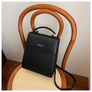 Detailed view of a black matte leather handbag on a minimalist wooden chair