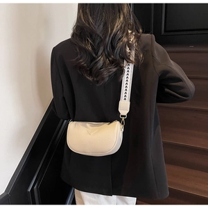 Close-up of cream pillow bag with wide textured strap shown on a model's shoulder