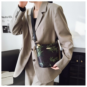 Detail of waterproof nylon crossbody bag featuring green botanical prints and gold zippers