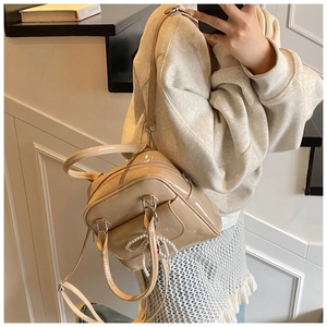 Beige patent leather handbag with pearl bow charm worn on a modern staircase
