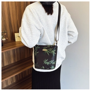 Detail of black nylon crossbody bag featuring green leaf patterns and gold logo plaque