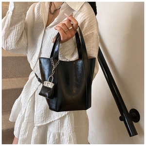 Detail of a black glossy PU leather bucket bag with a mini pouch on a silver chain