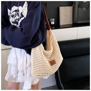 Close-up of cream woven shoulder bag with brown leather strap and logo detail