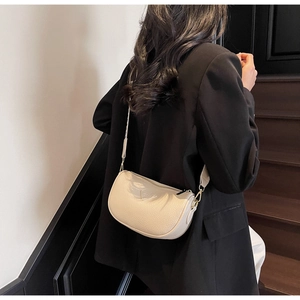 Close-up of off-white lychee leather crescent bag with adjustable strap on a model