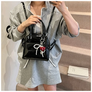 Detail of black patent leather bag with pearl bow and red heart charm on the straps