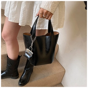 Detail of black glossy leather bucket bag with silver chain lock charm and tan lining
