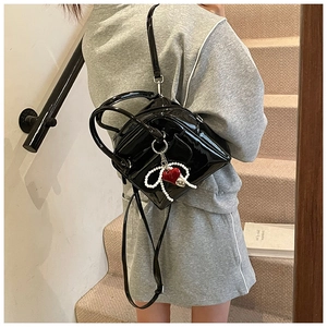 Glossy black mini backpack with pearl bow and red heart charm on sport casual outfit