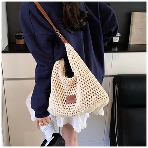 Detail of hollow woven tote bag with brown leather strap and brand patch
