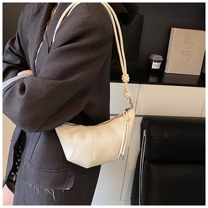 Detail of cream-colored crescent bag featuring vertical pleats and knotted shoulder strap