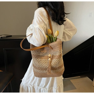 Détail du sac cabas en paille tressée avec pompon en perles de bois et bandoulière en cuir