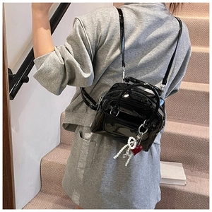 Detail of a black patent leather mini backpack with pearl heart charm on a model