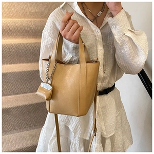 Detail of khaki bucket bag with dual handles, adjustable strap and mini pendant charm