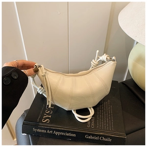 Close-up of cream croissant bag with stitched seams and knot detail on art books