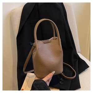 Detail of brown leather bucket bag with litchi grain texture on a white fabric chair