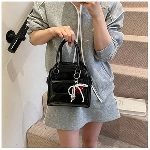 Detail of black glossy patent leather Boston bag with pearl heart charm held by a model