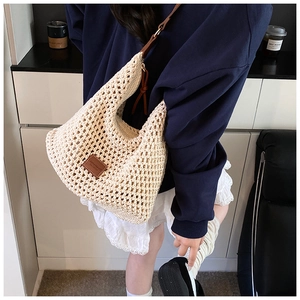Detail of cream hollow woven tote bag featuring brown leather strap and decorative label