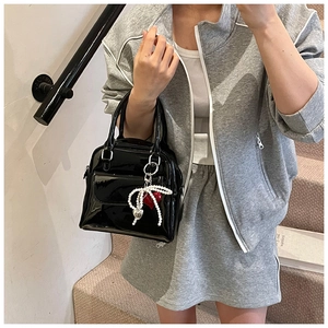 Detail of black patent leather handbag with pearl bow and heart charm on gray stairs