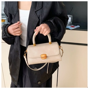 Detail einer cremefarbenen Vintage-Handtasche mit goldenem Verschluss und Ledergriff
