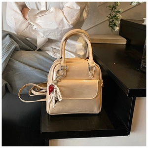 Detail of a beige patent leather handbag featuring pearl and heart pendant on black stairs