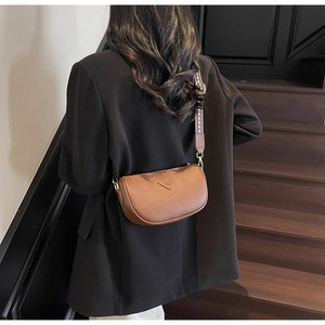 Brown lychee leather crossbody bag with wide jacquard strap worn over black blazer