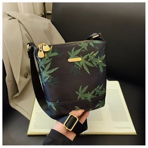 Detail of waterproof nylon shoulder bag with green leaf print and golden hardware accents