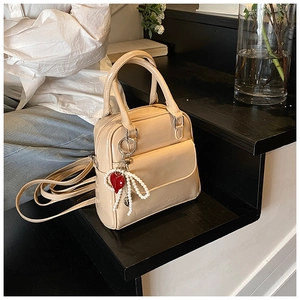 Detail view of beige patent leather handbag with glossy texture and pearl heart charm