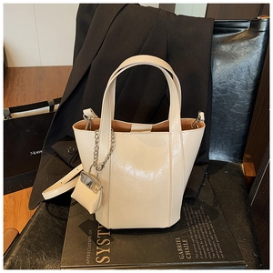 Detail of cream white bucket bag with glossy finish and mini purse chain charm accessory