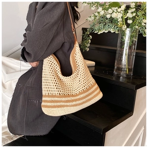 Close-up of a large beige knit tote bag with brown stripes on a model in grey coat