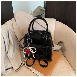 Detailed close-up of glossy black mini backpack with pearl bow and red heart pendant charm