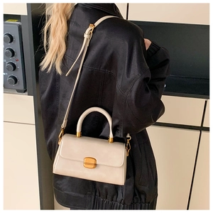 Schicke beige Umhängetasche in Quadratform mit goldenen Metallteilen über der Schulter