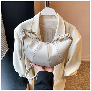 Detail of minimalist cream croissant bag with elegant knotted strap and curved stitching