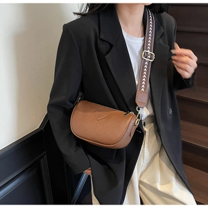 Detail of brown lychee grain leather pillow bag with wide geometric strap and metal plaque