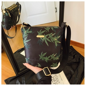Detailed view of black nylon crossbody bag with green leaf print and golden metal nameplate
