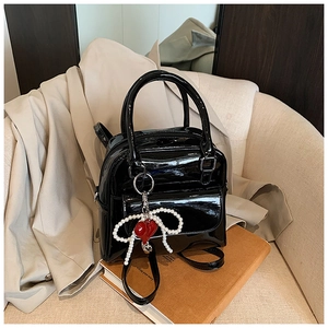 Detail of black patent leather bag with pearl bow and red heart charm on soft background