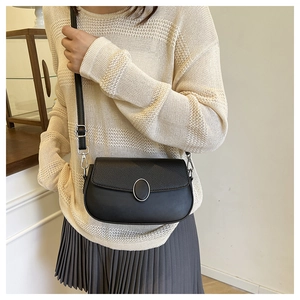 Close-up of minimalist black crossbody bag showing textured leather and silver oval buckle