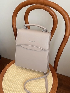 Minimalist light gray leather handbag with top handle on a rustic vintage chair