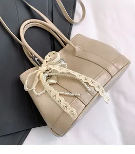 Détail du sac seau beige avec nœud en dentelle, perles et pendentif cœur