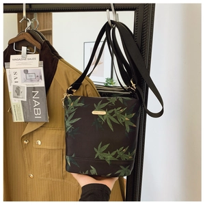Detailed view of black nylon bucket bag with green leaf print and golden metal logo
