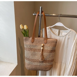 Détail du sac cabas en paille tressée avec anses en cuir marron et pompons en perles