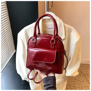 Detail shot of a dark red patent leather multi-way handbag with glossy mirror finish