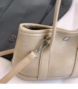 Gros plan détaillé sur la boucle argentée et les coutures du sac seau en similicuir beige