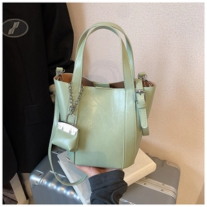 Detail view of a pea green bucket bag in shiny synthetic leather with silver padlock charm