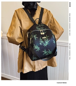 Detailed view of women's backpack featuring green leaf pattern and golden zipper closures