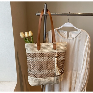 Détail d'un sac cabas en paille tissée avec anses en cuir marron et pompon décoratif
