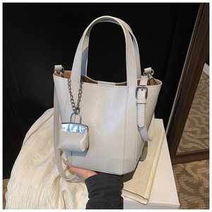 Detail view of cream bucket bag with shiny synthetic leather and silver lock pendant