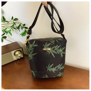 Detail view of water-resistant nylon bucket bag with green leaf prints and gold zippers
