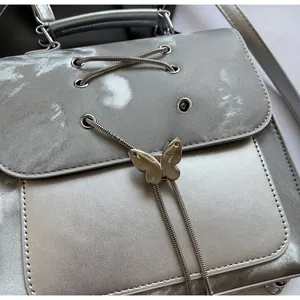 Detail of silver metallic backpack featuring a butterfly buckle and woven cord accents