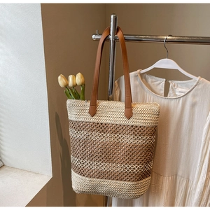 Détail du sac cabas en paille avec anses en cuir marron et texture tissée sur un cintre
