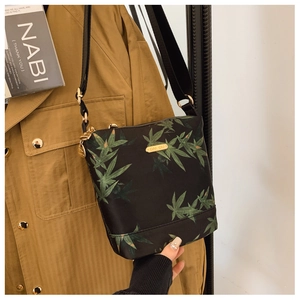 Detail of waterproof black nylon bag with green leaf print and golden hardware on a trench coat