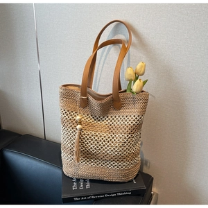 Détail d'un sac cabas en paille tissée avec anses en cuir marron et pompons en bois